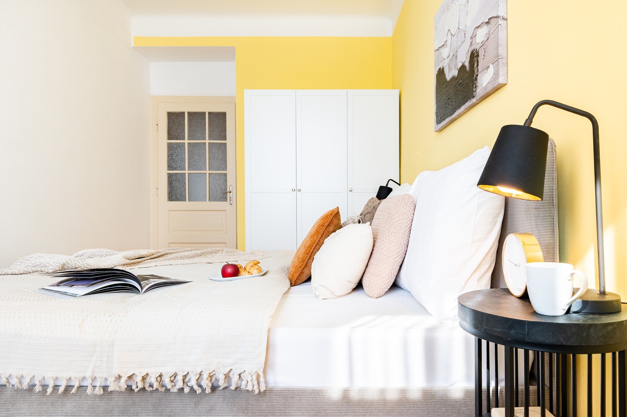 Prostor je svěží, optimistický a harmonický, s teplým žlutým akcentem, vrstvenými textiliemi a detaily, které z ložnice dělají útulné, ale zároveň moderní místo k odpočinku.